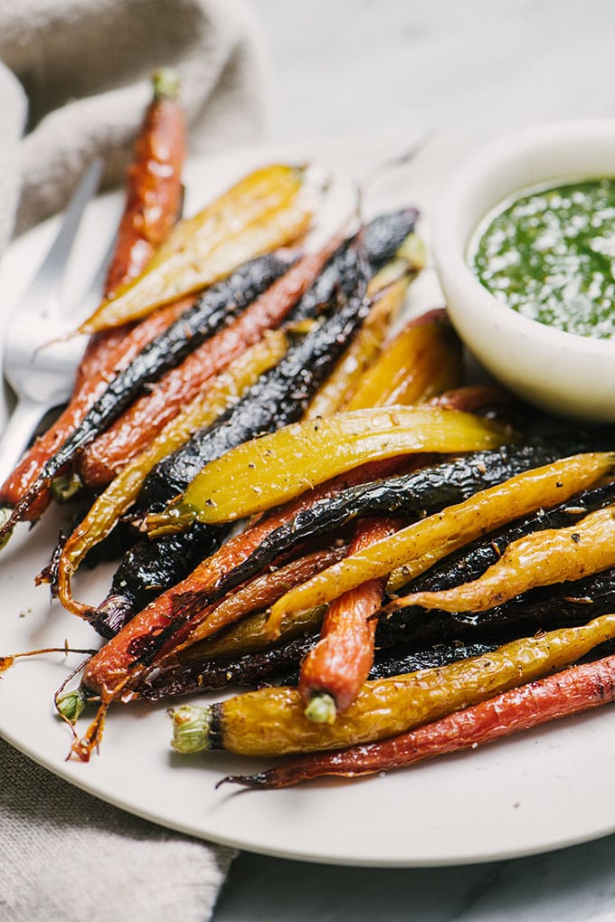 A white plate filled with honey roasted carrots and a small bowl of carrot green pesto.