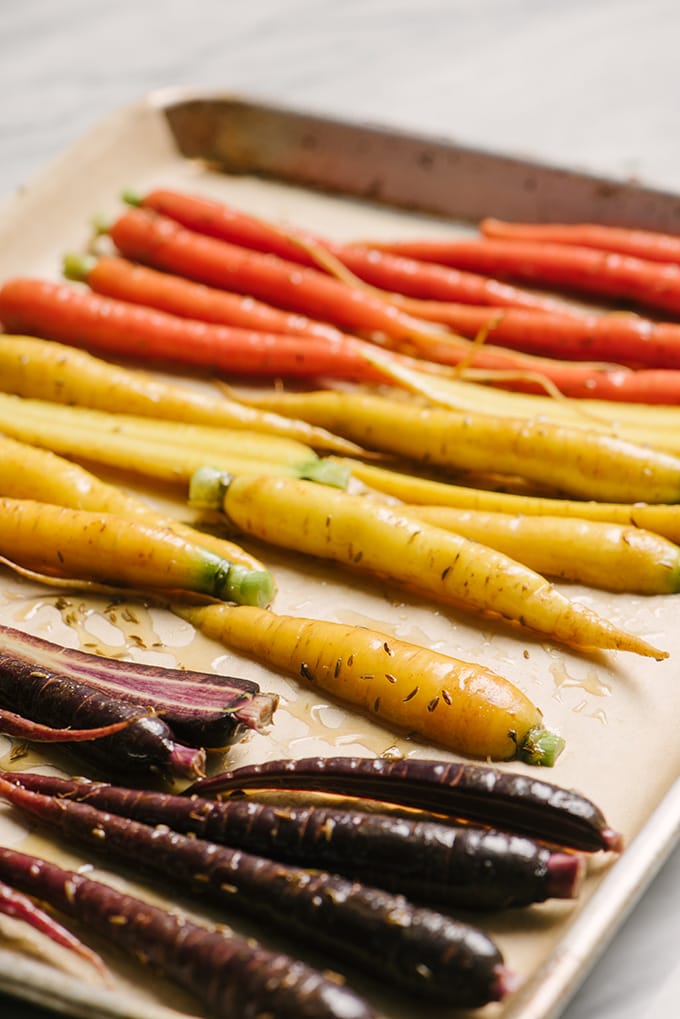 Tri-color carrots tossed with honey and cumin on a baking sheet.