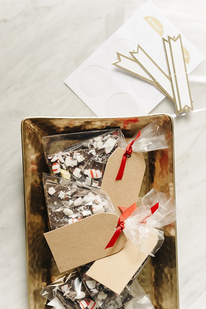 Homemade chocolate bark edible Christmas gift wrapped in pretty packaging on a gold tray.