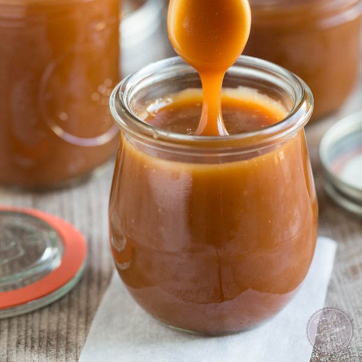 Homemade salted caramel sauce drizzling off a spoon into a jar.