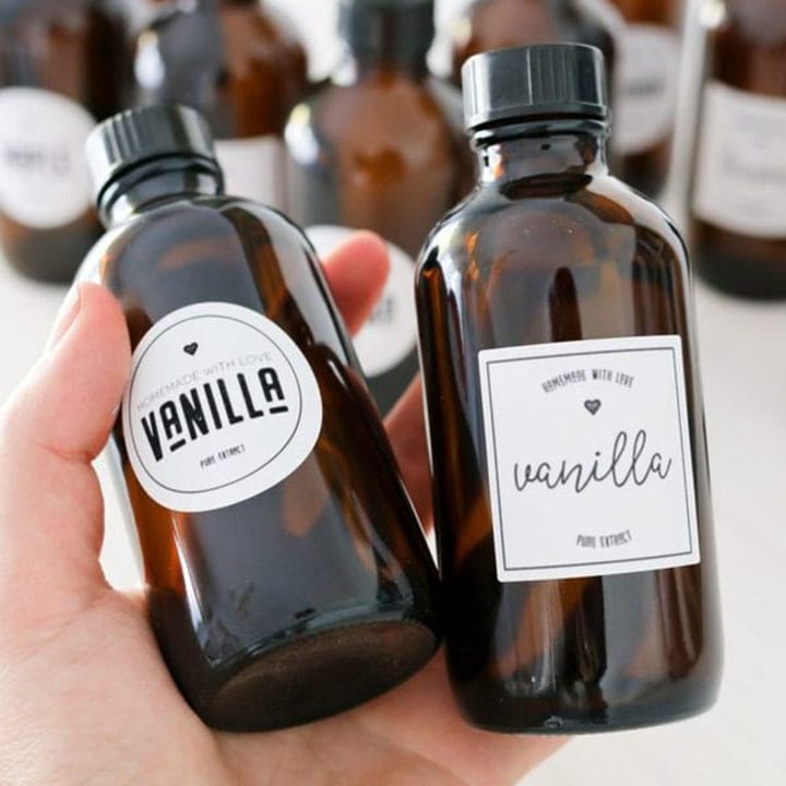 A woman's hand holding two jars of homemade Instant Pot Vanilla Extract.
