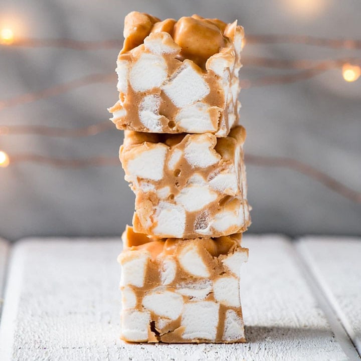 A stack of butterscotch peanut butter marshmallow bars on a white table with twinkle lights in the background.