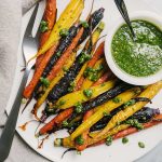 A plate of tricolor honey roasted carrots drizzled with carrot green pesto.