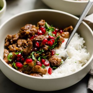 A bowl of paleo pomegranate chicken braised with walnuts and coconut milk served over white rice garnished with parsley and pomegranate seeds.
