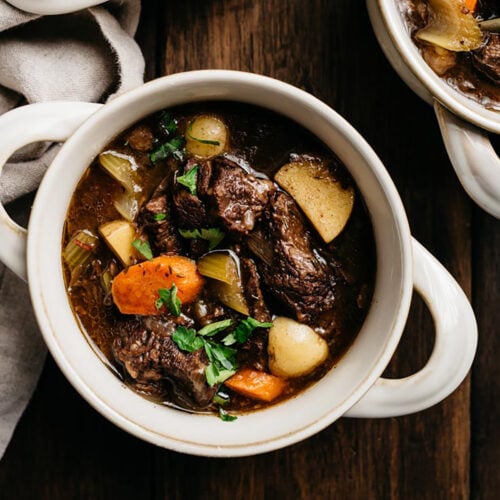 Red wine beef stew in a bowl garnished with fresh parsley on a wood background.