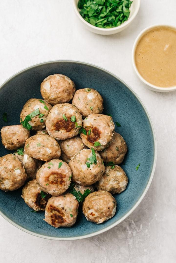A blue serving bowl of baked turkey meatballs with a bowl of onion gravy on the side.