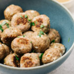 Side view, baked turkey meatballs in a blue bowl garnished with parsley.