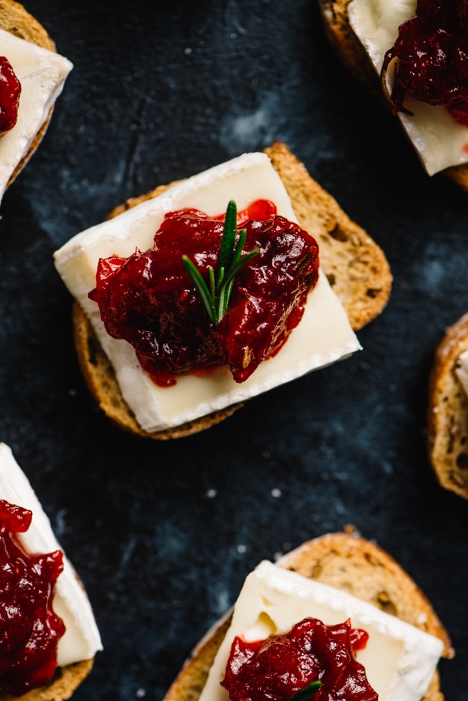 An overhead view of cranberry brie crostini arranged on a black chalkboard background.