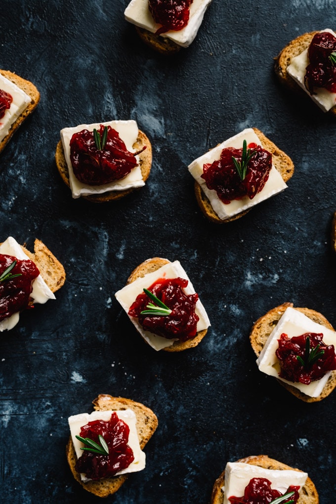 An overhead view of a spread of cranberry brie bites on a black chalkboard background.
