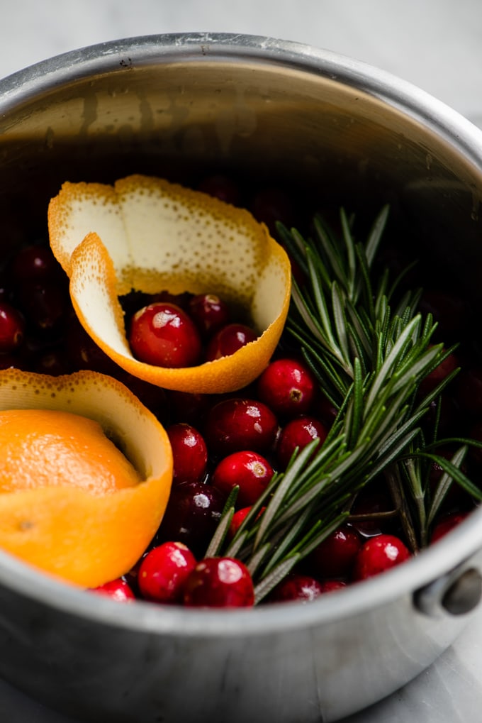 Fresh cranberries, brown sugar, orange zest, and fresh rosemary in a small pot for making homemade cranberry jam.