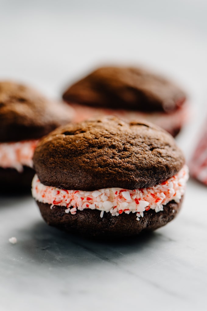 A close-up image of a peppermint whoopie pie holiday dessert with buttercream frosting and crushed candy canes. 