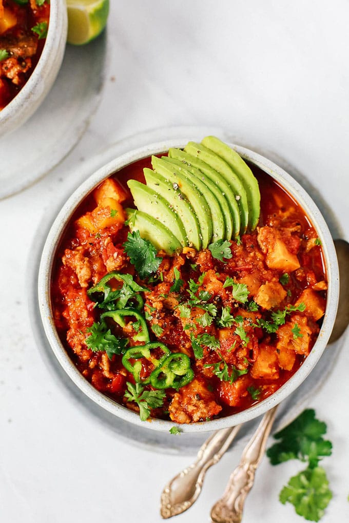 A bowl of easy sweet potato whole30 chili garnished with avocado, cilantro, and jalapeno on a marble background.