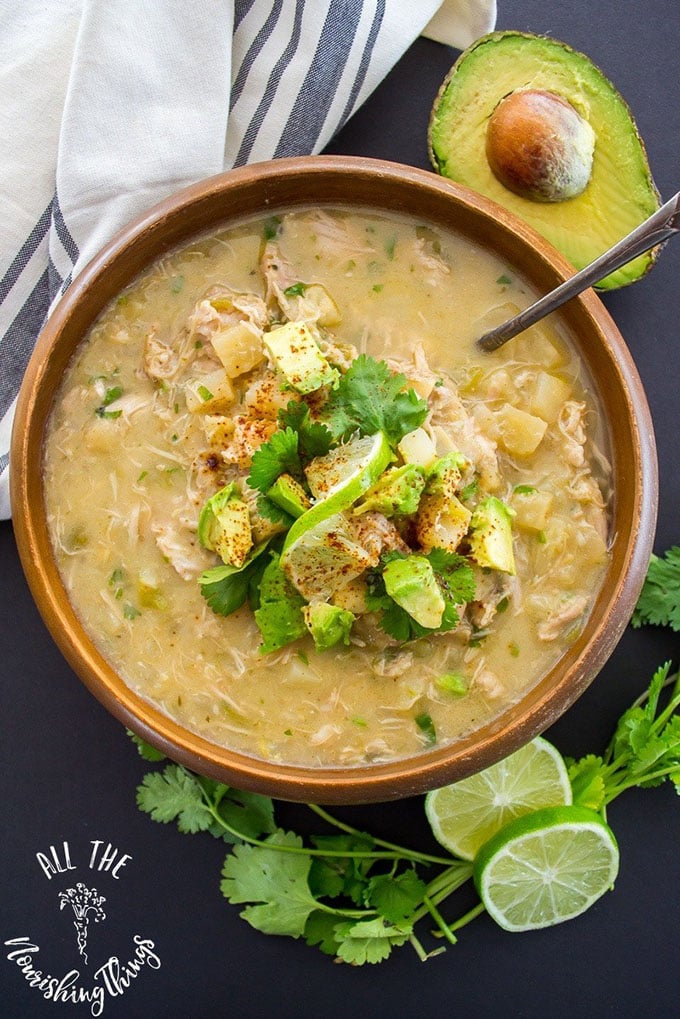 Green chicken chili whole30 soup in a brown bowl with avocado, lime, and cilantrol