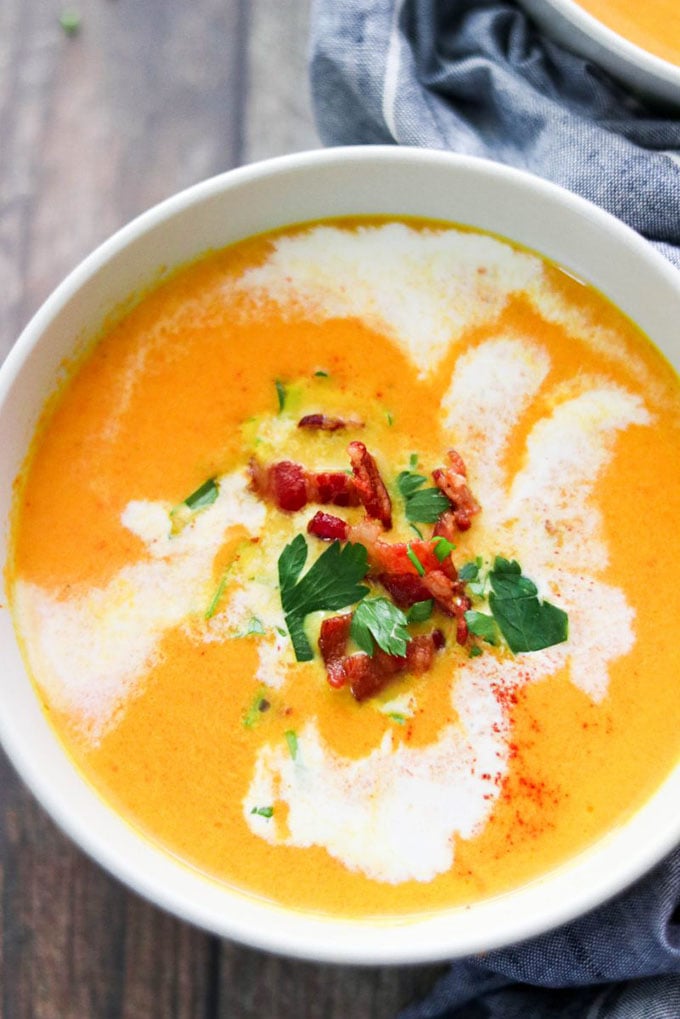 A white bowl of creamy paleo carrot whole0 soup with bacon and coconut cream.
