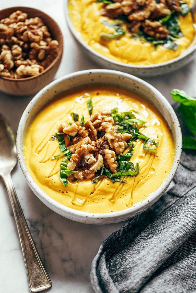 Golden turmeric vegetable whole30 soup in a white bowl garnished with walnuts and basil.