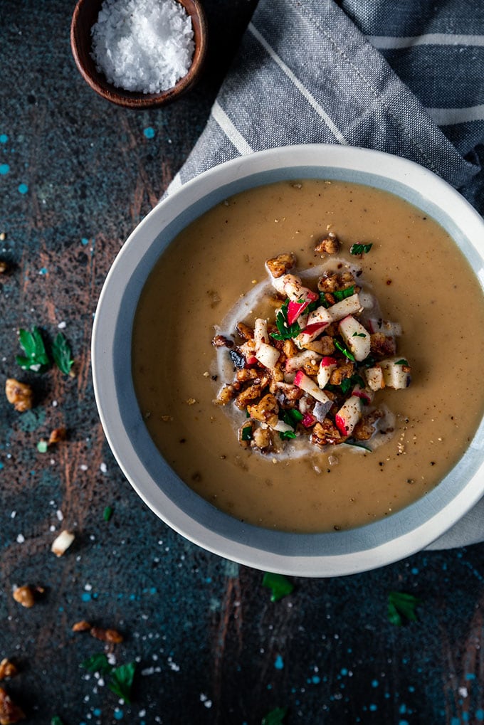 A bowl of creamy moroccan spiced parsnip whole30 soup on a dark background garnished with apples and za'atar spice.