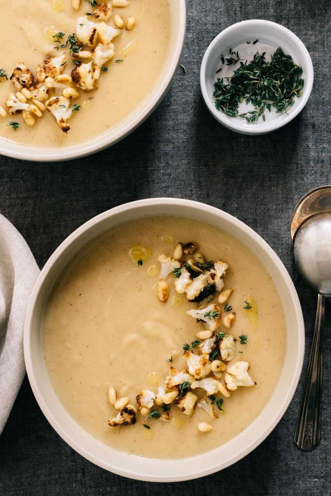 A bowl of creamy roasted garlic and cauliflower whole30 soup garnished with thyme and cauliflower florets.