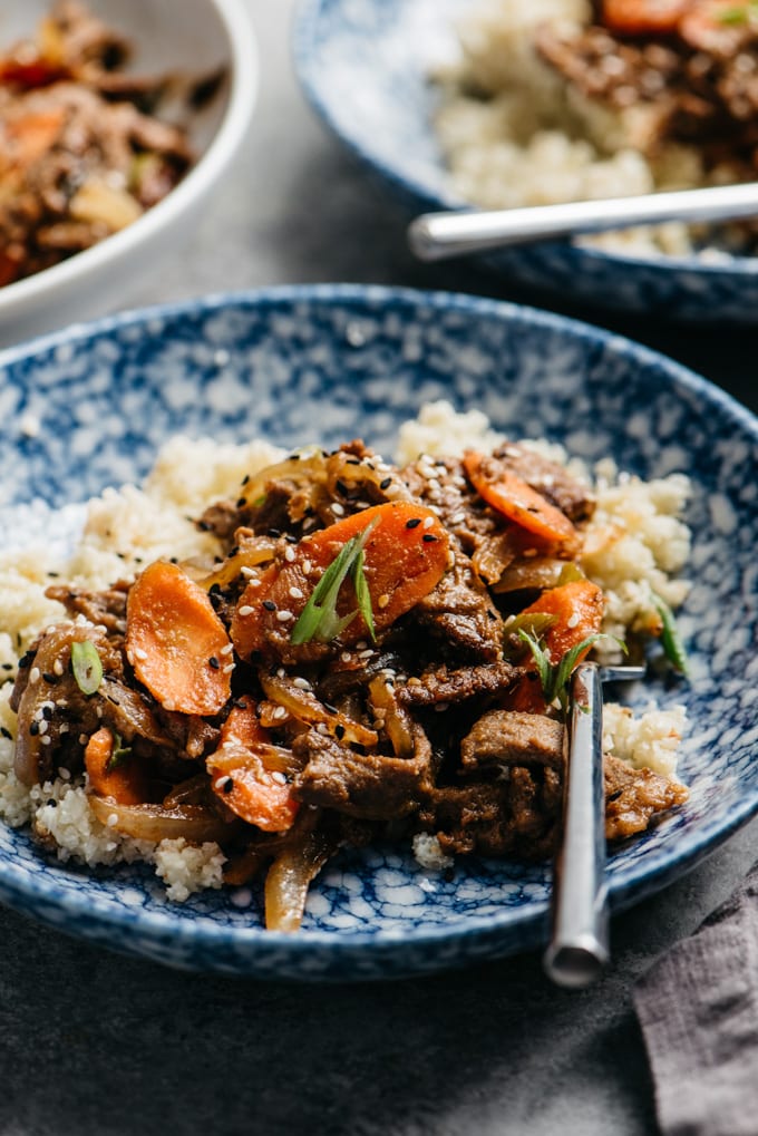 A bowl of healthy Whole30 beef bulgogi over cauliflower rices in a blue bowl with a silver fork.