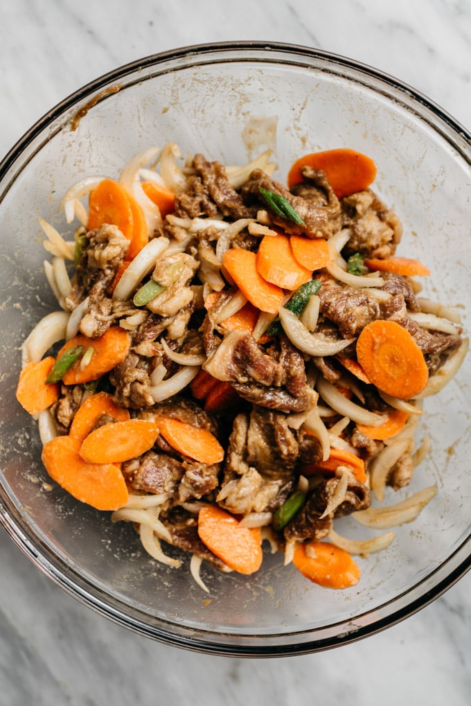 Whole30 bulgogi marinated sirloin in a mixing bowl tossed with onions, carrots, and green onions before being stir fried.