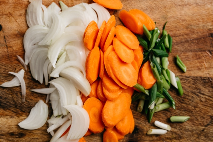 Thinly sliced sweet onion, sliced carrots, and chopped green onions on a cutting board for making healthy whole30 beef bulgogi.
