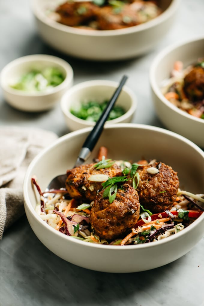 A bowl of whole30 ginger pork poppers with citrus asian slaw on a marble table.