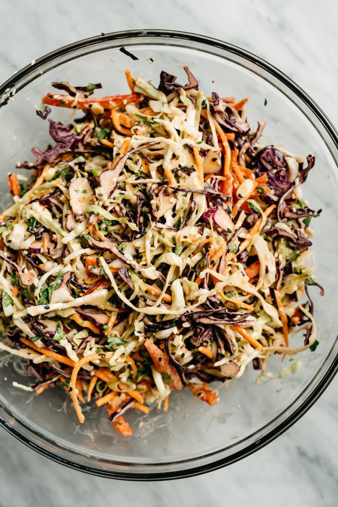 Citrus asian slaw ingredients tossed with dressing in a glass bowl.
