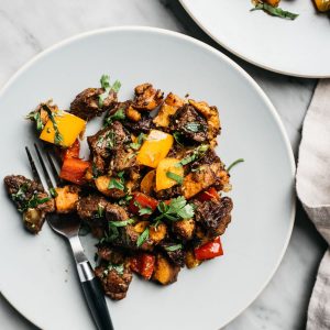 Whole30 steak bites sauteed with sweet potatoes and bell peppers on a blue plate with a black fork.