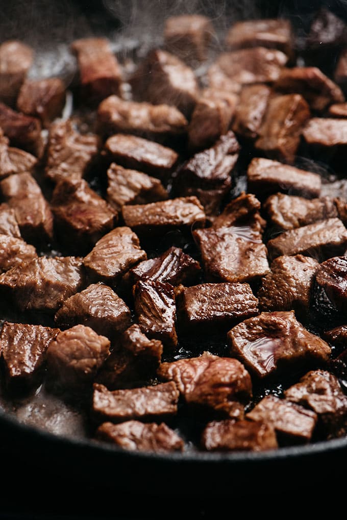 Seared pieces of diced flat iron steak in a cast iron skillet for making Whole30 steak bites.