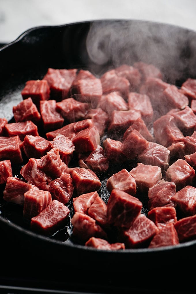 Diced pieces of raw flat iron steak in a cast iron skillet.