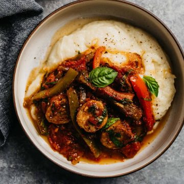 A bowl of healthy italian sausage and peppers over gluten free cauliflower puree on a cement background with a grey linen napkin.