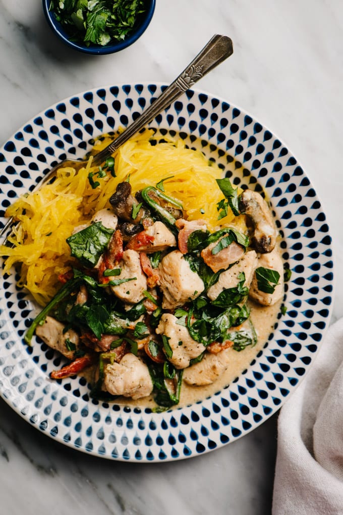 A plate of healthy tuscan chicken with creamy dairy free bacon sauce over spaghetti squash on a marble table with a linen napkin.