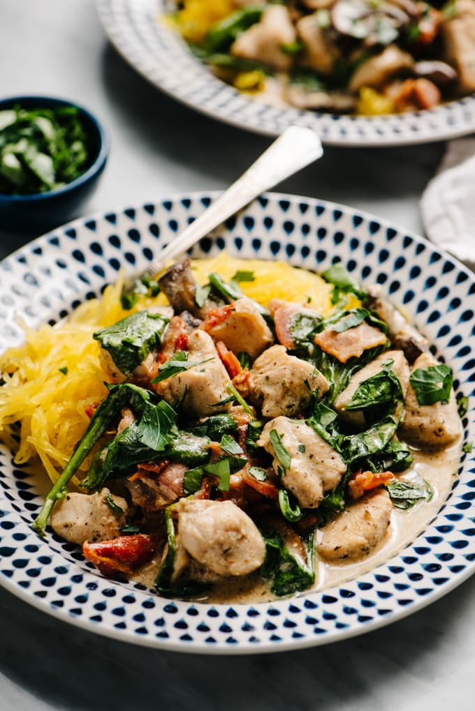 Two plates of healthy tuscan chicken with creamy dairy free sauce over spaghetti squash on a marble table with a small dish of fresh parsley on the side.