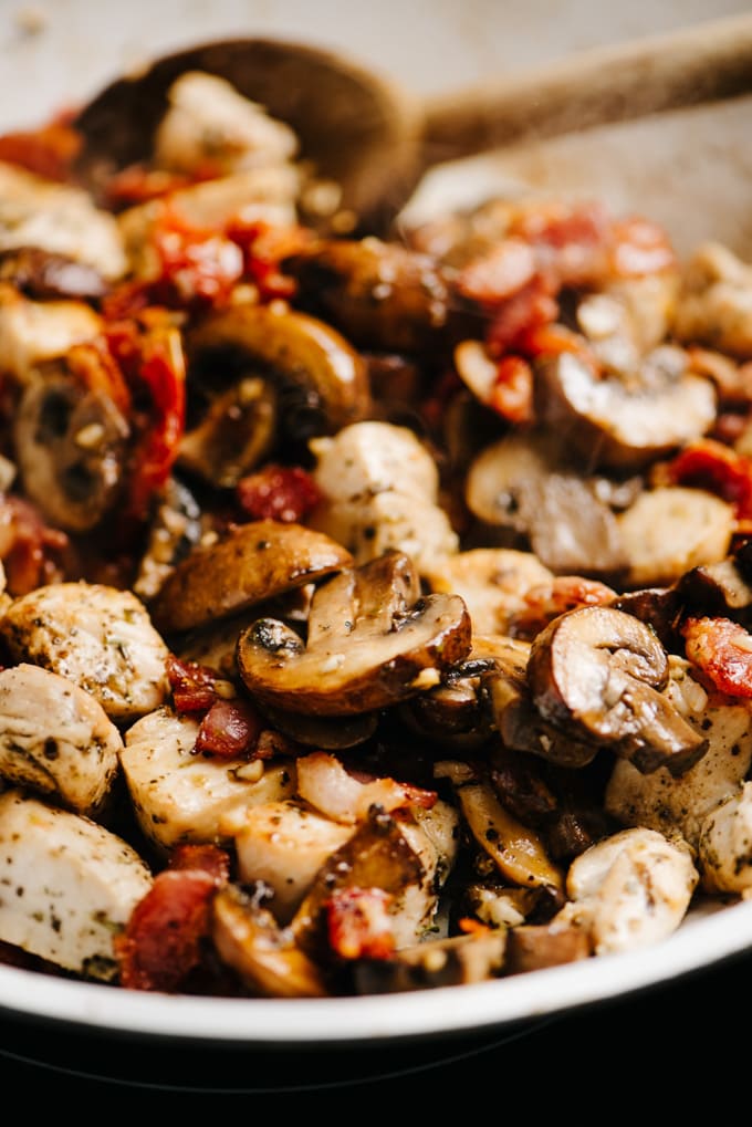 Diced tuscan chicken with sun dried tomatoes, bacon, and mushrooms in a skillet.