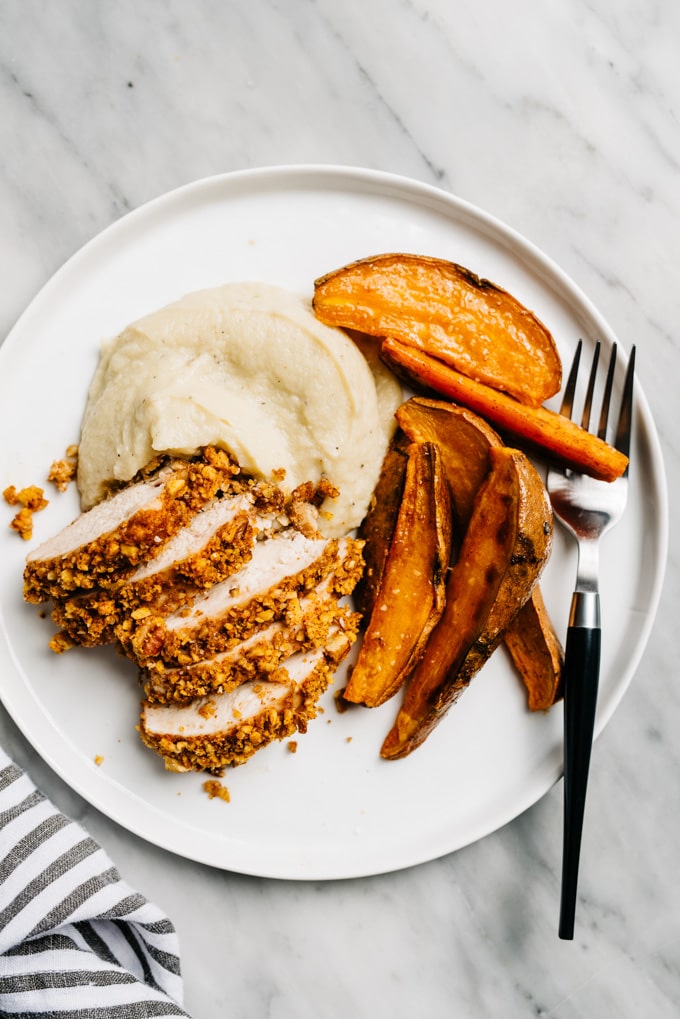 Easy pecan sheet pan chicken dinner on a plate - sliced pecan chicken over cauliflower puree with sweet potato fries.