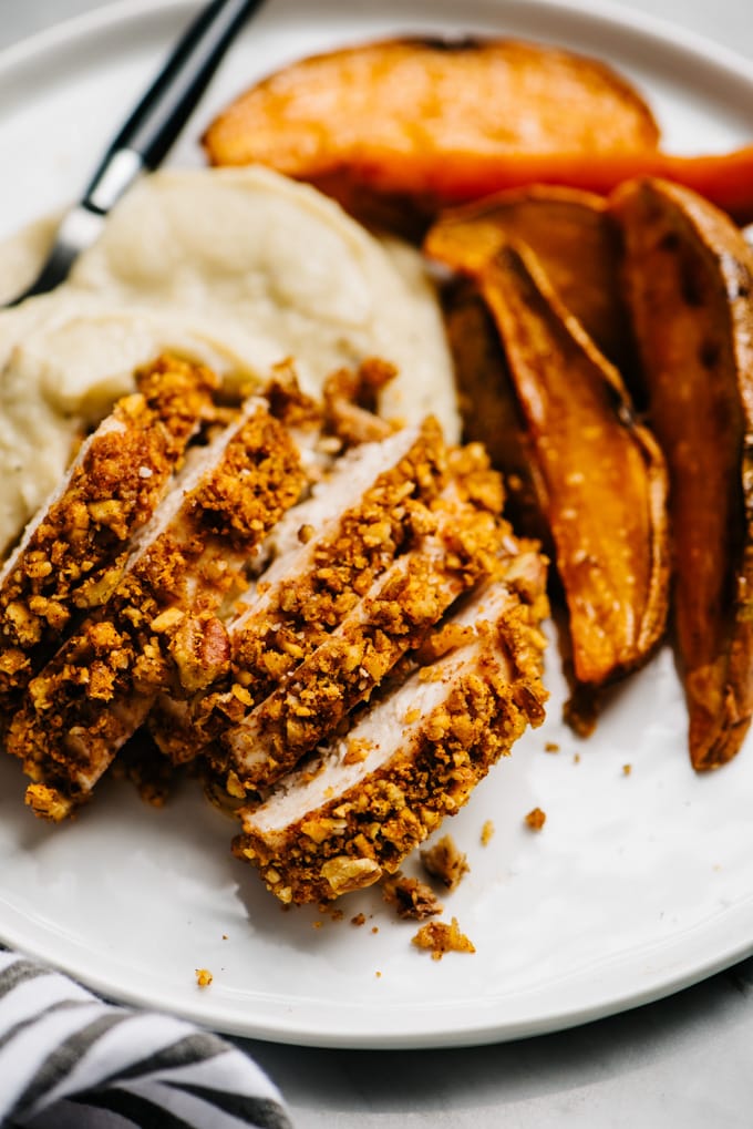 Whole30 and gluten free baked pecan chicken with sweet potato fries and cauliflower mash on a white plate.