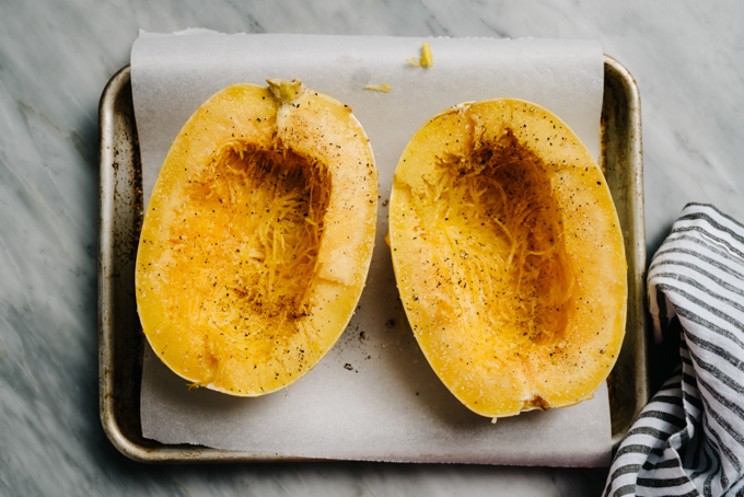 A large spaghetti squash sliced in half, seeds removed, and rubbed with olive oil on a baking sheet.