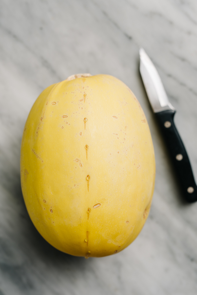 A large spaghetti squash scored down the center on a marble table.