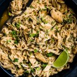 A serving bowl of Whole30 chicken lime chicken with a lime wedge and serving spoon.