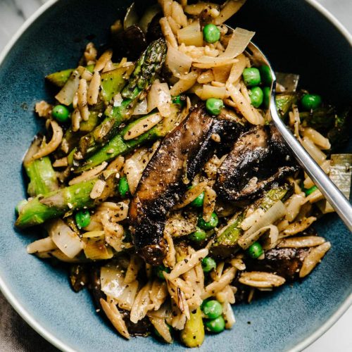 Vegan lemon orzo pasta in a blue bowl with asparagus, mushrooms, and peas.