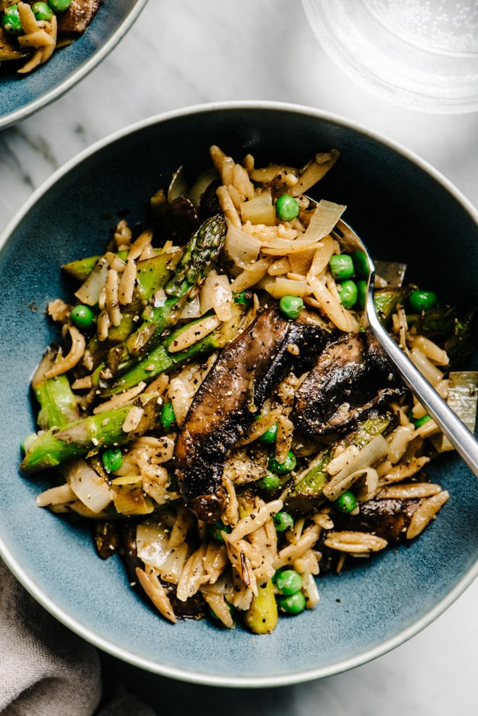Vegan lemon orzo pasta in a blue bowl with asparagus, mushrooms, and peas.