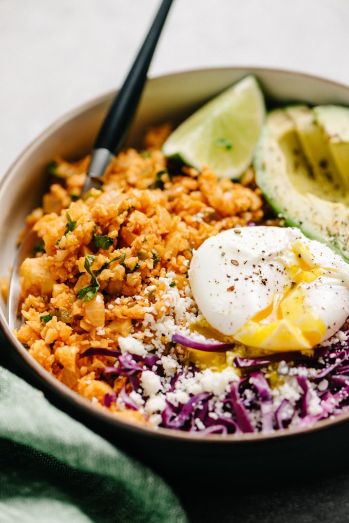 Mexican cauliflower rice keto bowl with avocado, poached egg, cabbage, and queso fresco.