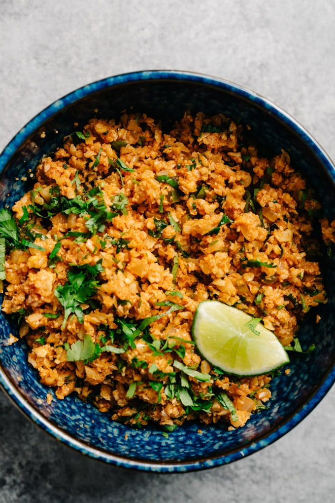 A bowl of vegan mexican cauliflower rice with cilantro and a lime wedge.