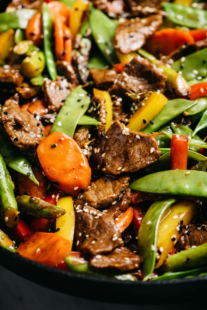 Side view, stir fried beef and vegetables in a cast iron skillet garnished with sesame seeds.