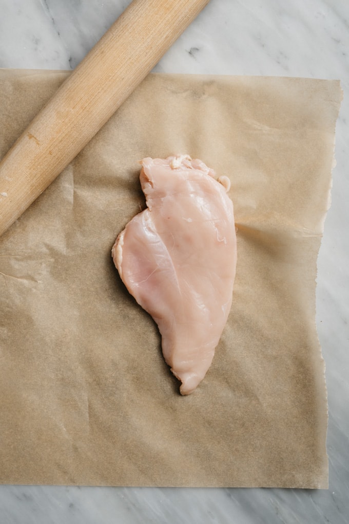 A chicken breast pounded to even thickness on a piece of parchment paper.