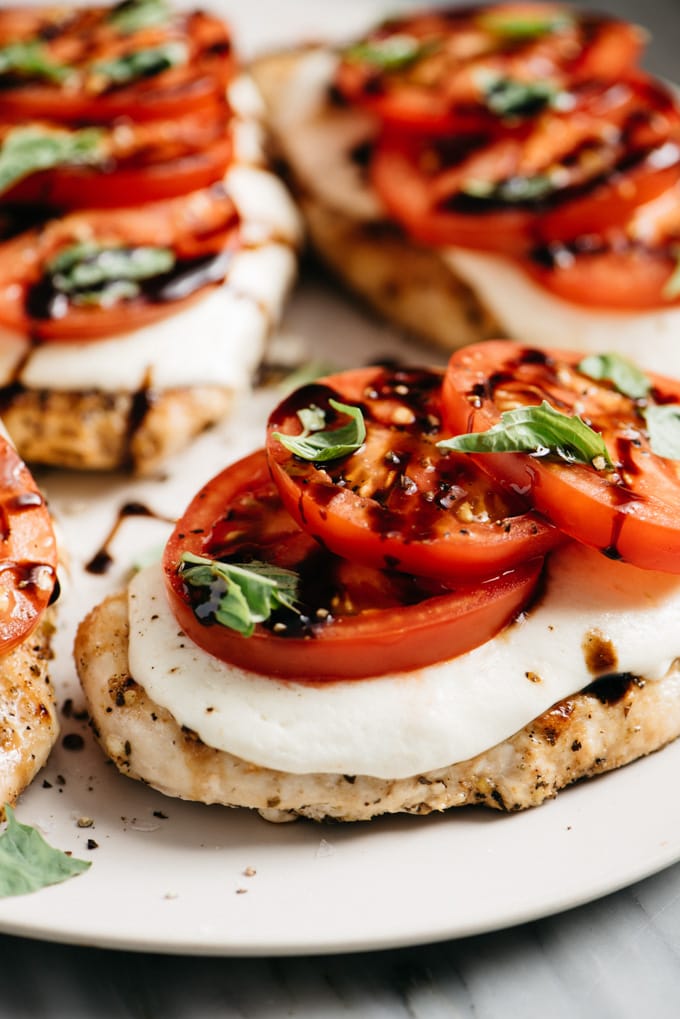 A close-up image of caprese chicken with mozzarella, fresh tomatoes, basil, and balsamic.