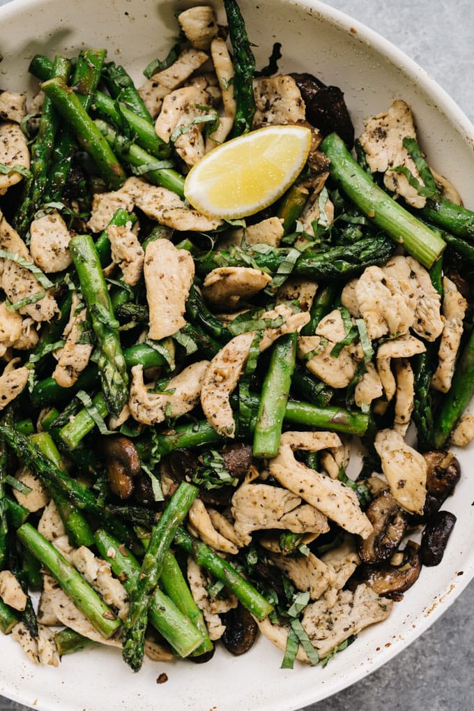 Whole30 and paleo chicken and asparagus recipe in a skillet with mushrooms, lemon and basil.