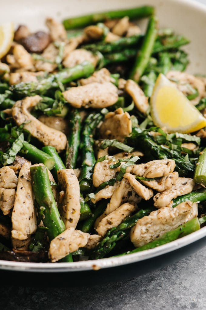 Whole30 chicken and asparagus dinner recipe in a skillet on a cement background.