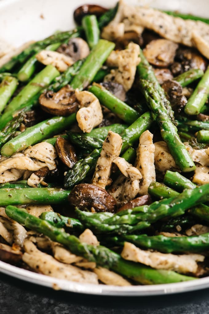 Chicken and asparagus recipe in a skillet with lemon, basil, and mushrooms.