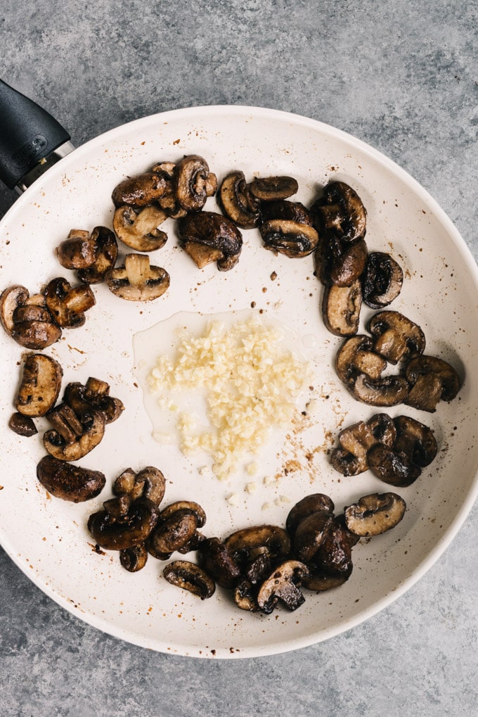 Garlic cooking in the center of a skillet surrounded by sautéed mushrooms.