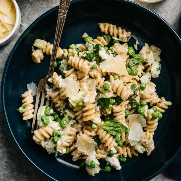 Easy weeknight ricotta pasta with peas in a blue bowl with a side of parmesan cheese.